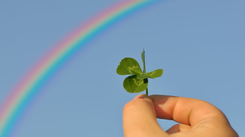Holding-out-a-four-leaf-clover-to-the-blue-sky-with-a-rainbow-over-it