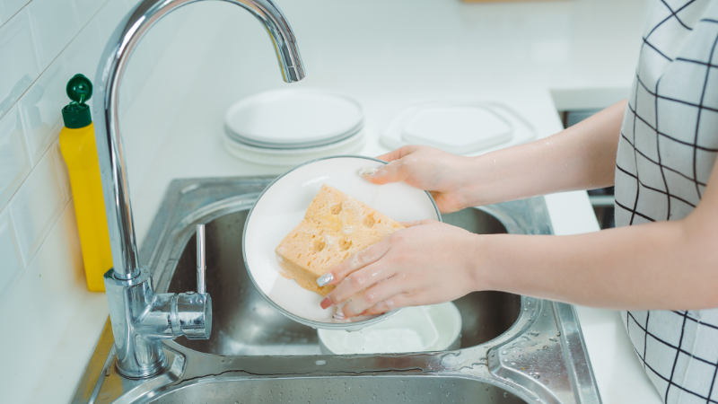 A-person's-hand-washing-dishes-with-a-sponge