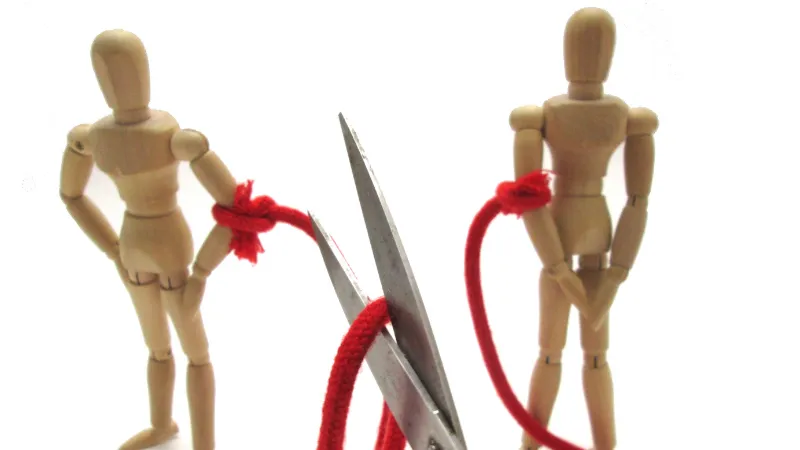 2つの人形を繋ぐ赤い糸をはさみで切ろうとしている