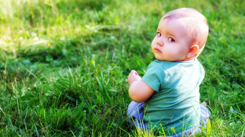 芝生の上にしゃがみ、こちらを振り返る赤ちゃん