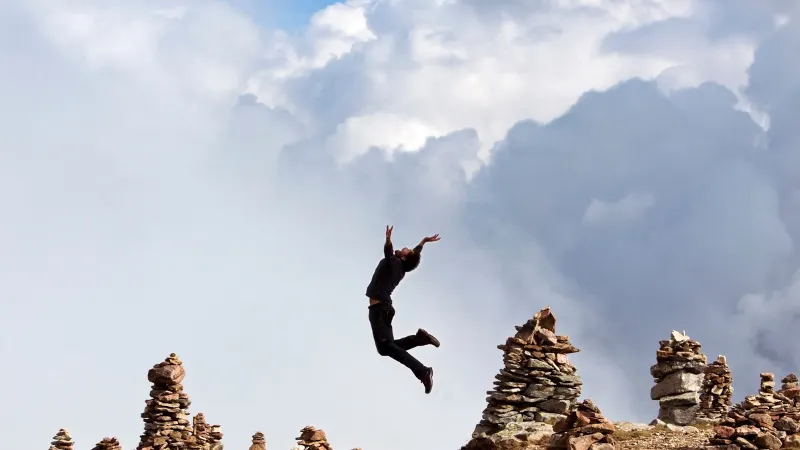岩が積みあがった山の上で空に向かってジャンプする男性
