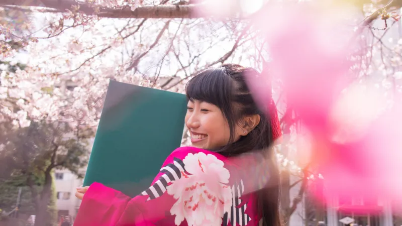 桜が咲く木の下で満面の笑みで振り返る、卒業式を迎えた袴姿の女の子