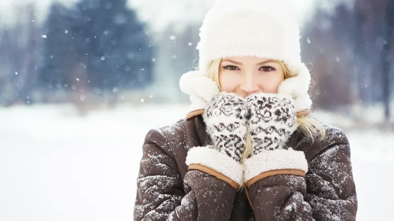 雪が降る中、手袋や帽子や防寒着を着て笑顔の女性