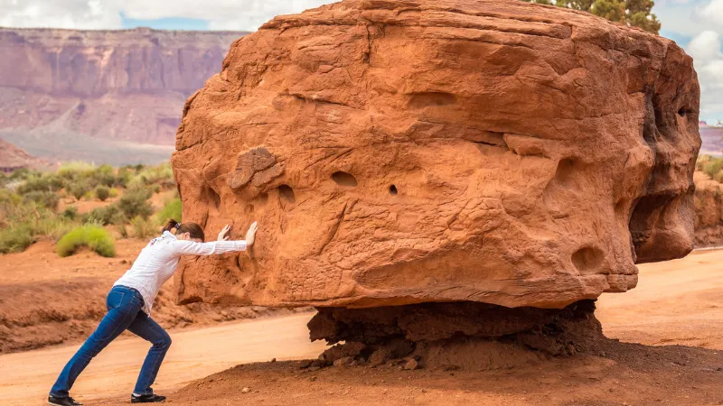 大きい岩を動かそうと、岩を押している女性